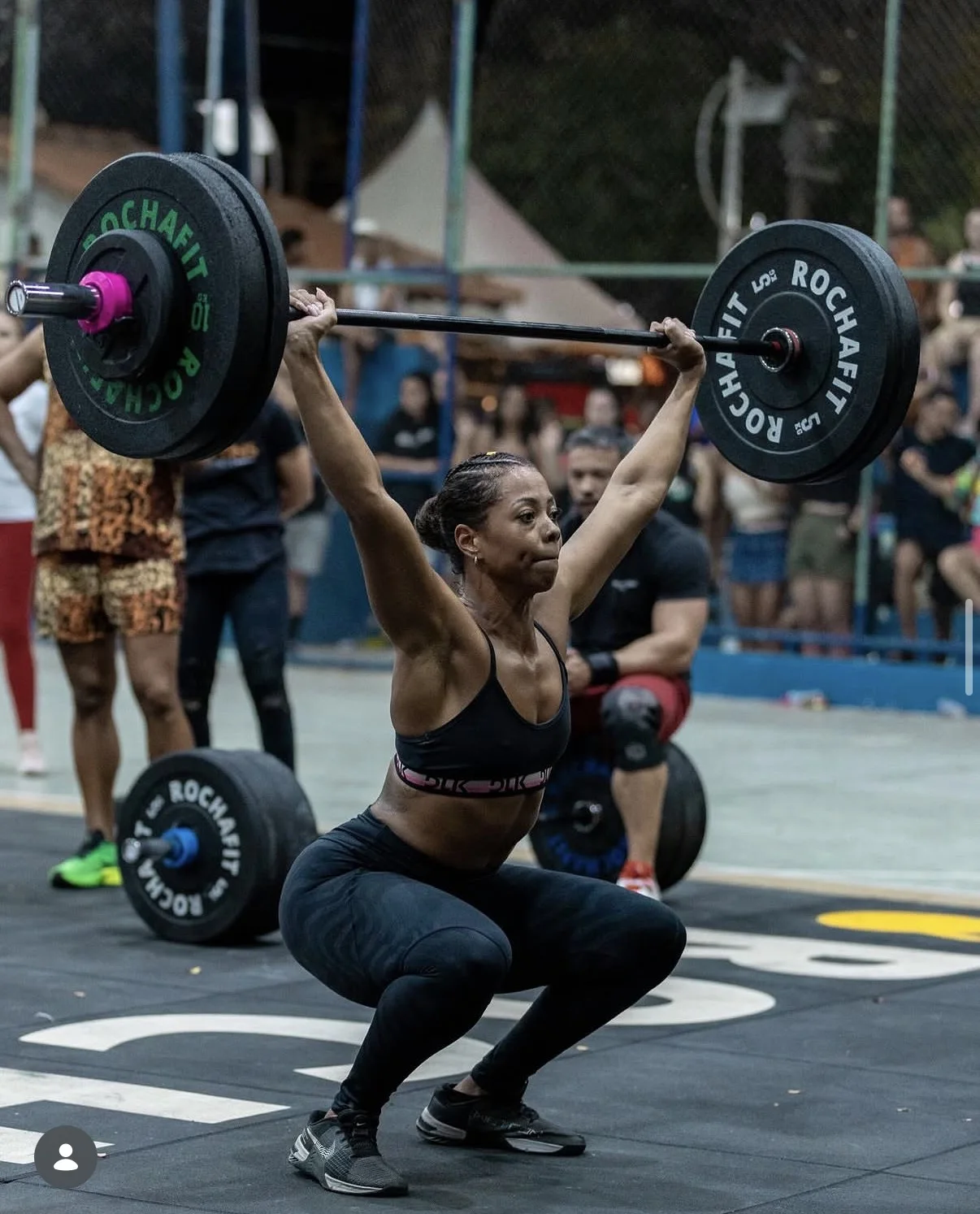 Atleta em agachamento com a barra acima da cabeça